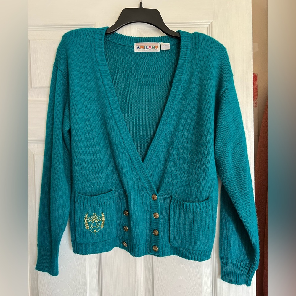 Cardigan style sweater with pockets, gold buttons and gold emblem.
